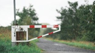 Rood-witte slagboom bij een onverharde weg in de regen