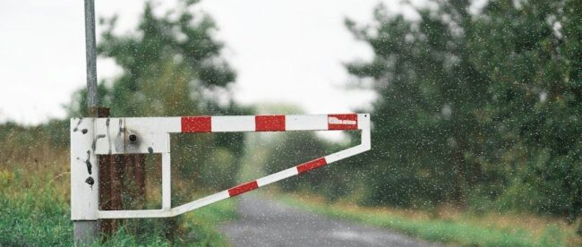Rood-witte slagboom bij een onverharde weg in de regen